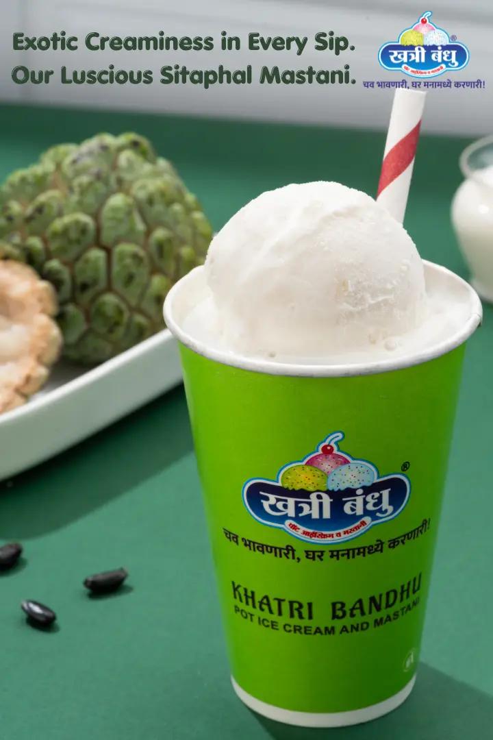 A tall glass of Sitaphal Mastani topped with thick ice cream, made with fresh custard apples, set against a festive background.